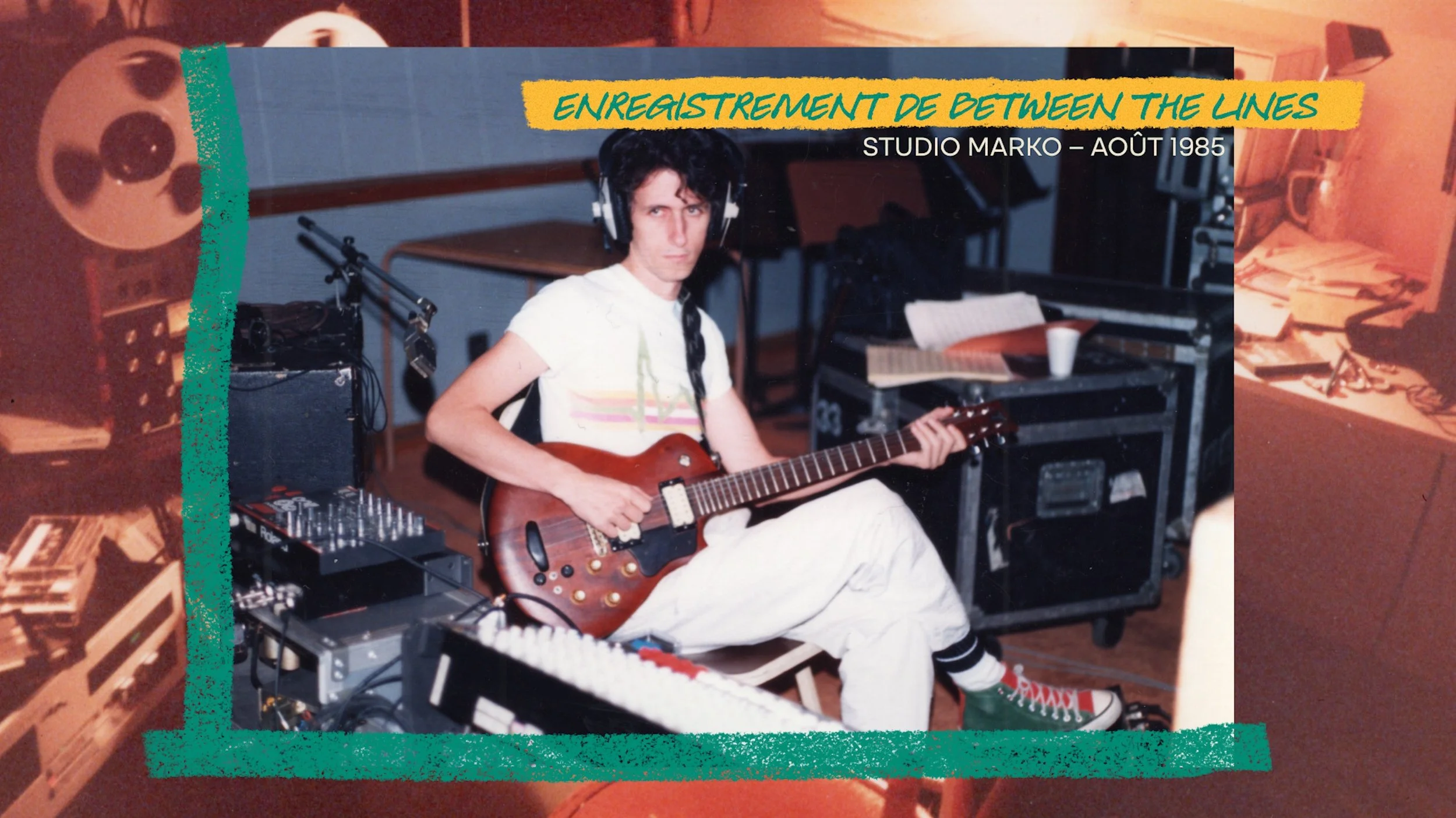 Photo d'un jeune homme jouant de la guitare dans un studio d'enregistrement, avec des équipements audio, des papiers, un ordinateur portable et une tasse en carton en arrière-plan.
