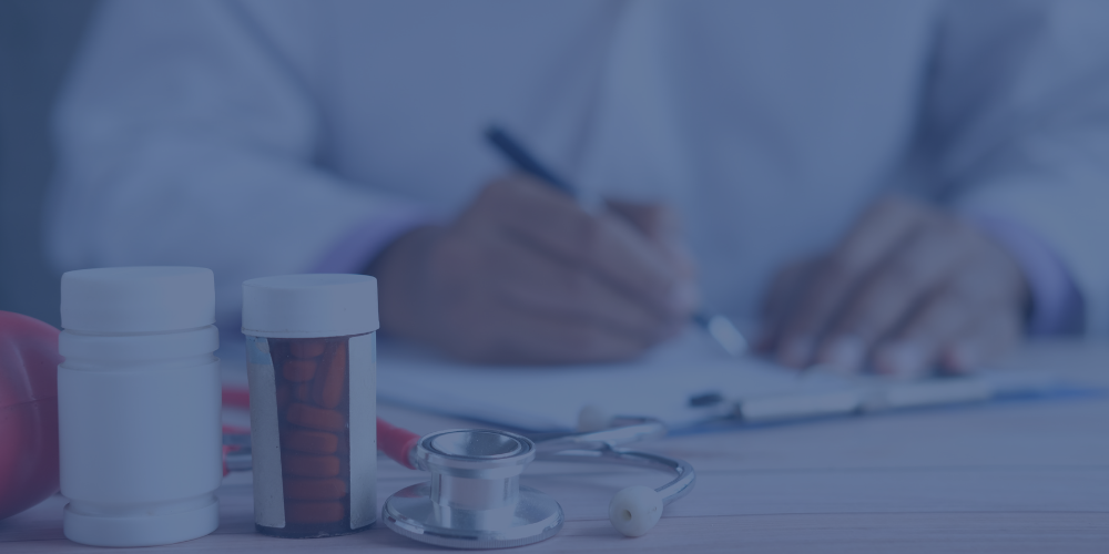 Close-up of prescription bottles and a stethoscope on a medical table, with a person in a white coat writing in a notebook in the background.