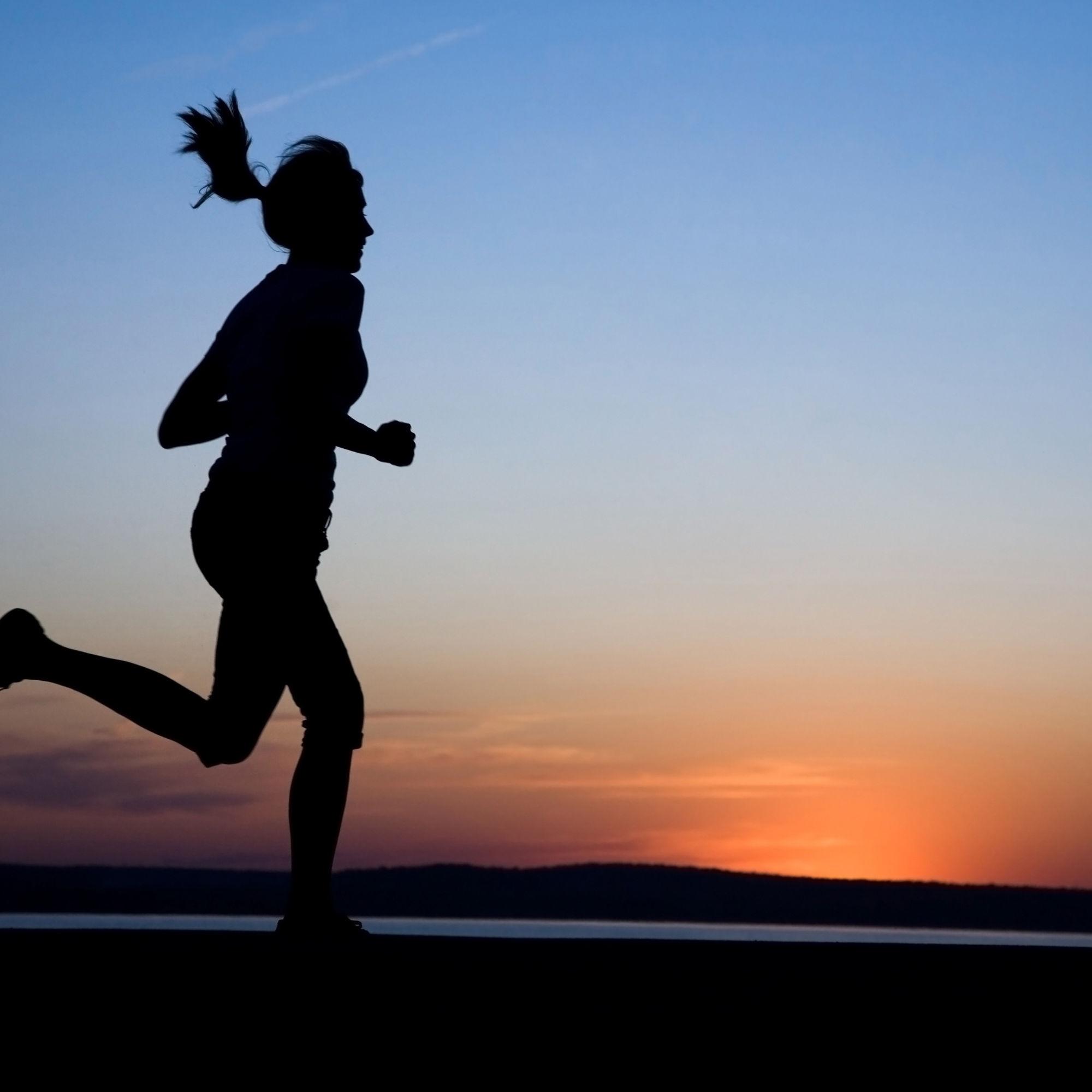 Silhouette of a person running at sunset or sunrise with a colorful sky in the background.