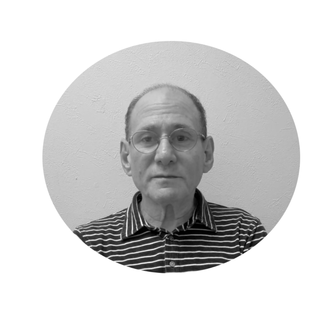 Black and white portrait of a middle-aged man with glasses, wearing a button-up shirt with horizontal stripes, standing against a textured wall.