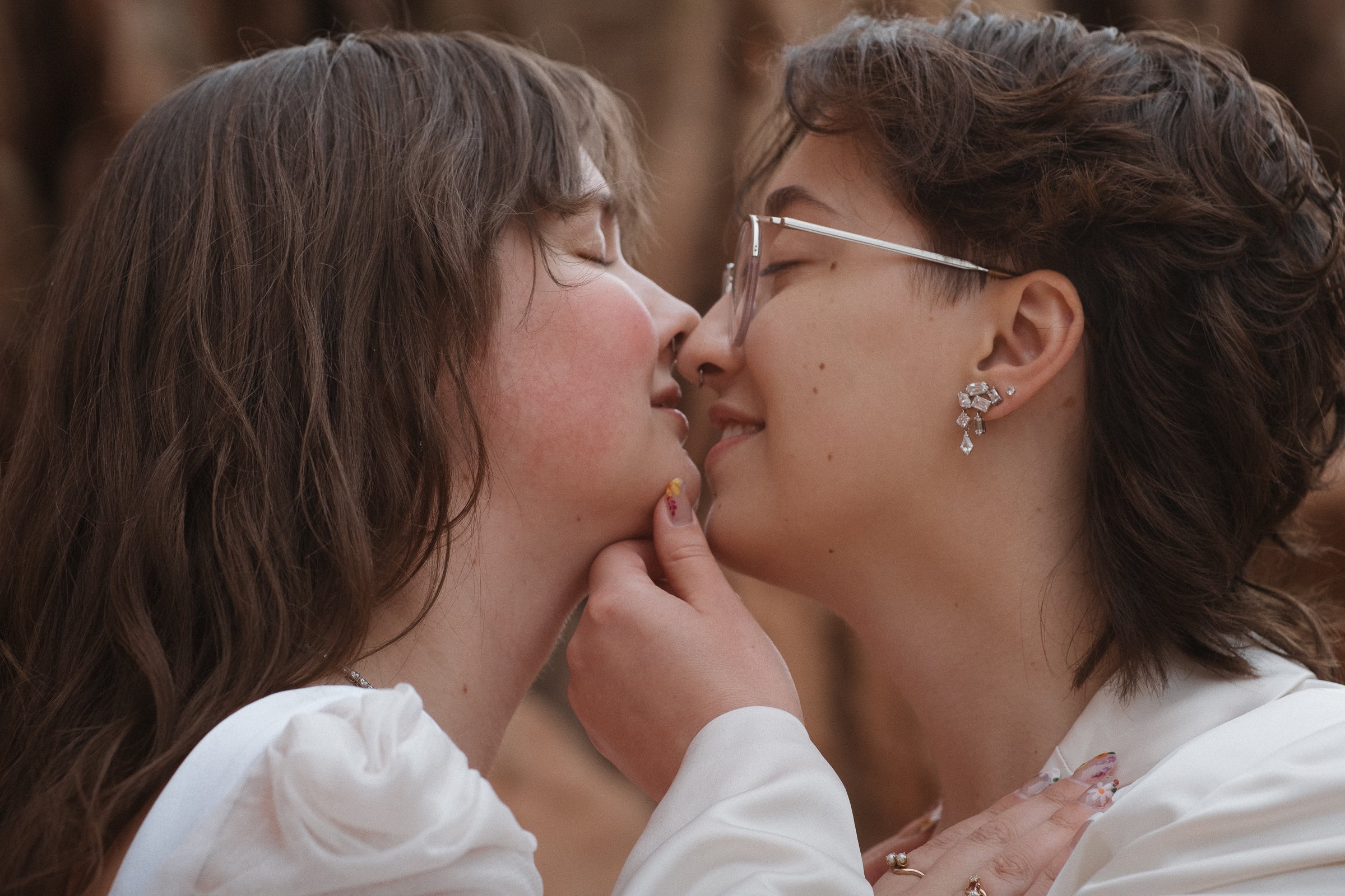Two women are about to kiss, touching foreheads and noses, with one gently holding the other's chin.