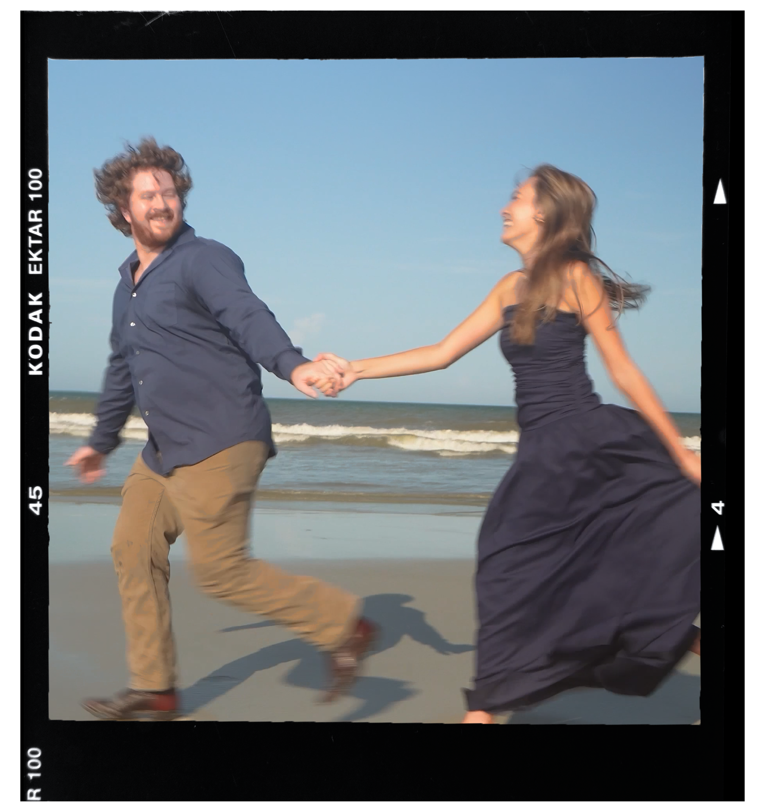 A man and a woman holding hands and running on the beach, smiling and laughing, with ocean waves in the background.
