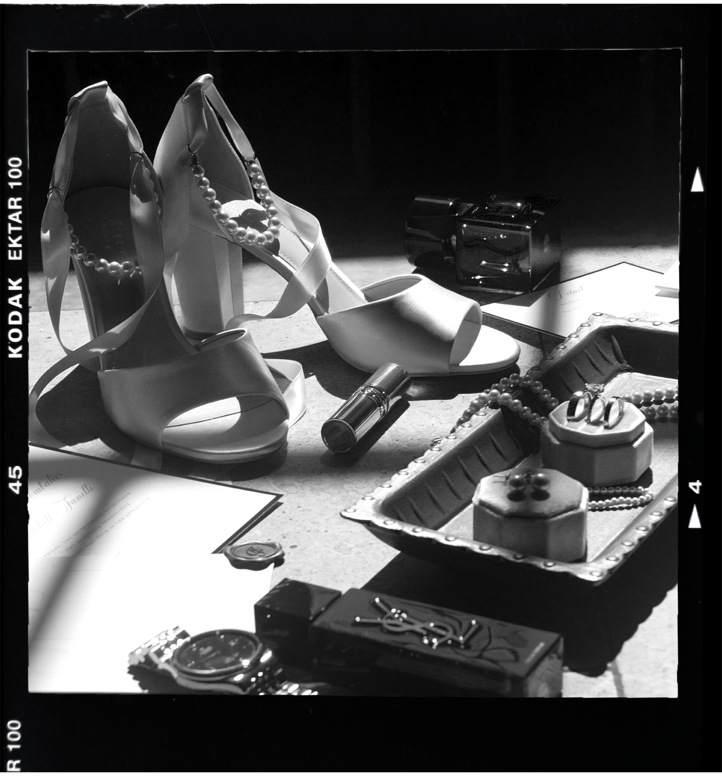 Women's shoes with pearl necklaces, jewelry, a lipstick, a watch, and a tray of rings and earrings arranged on a surface.