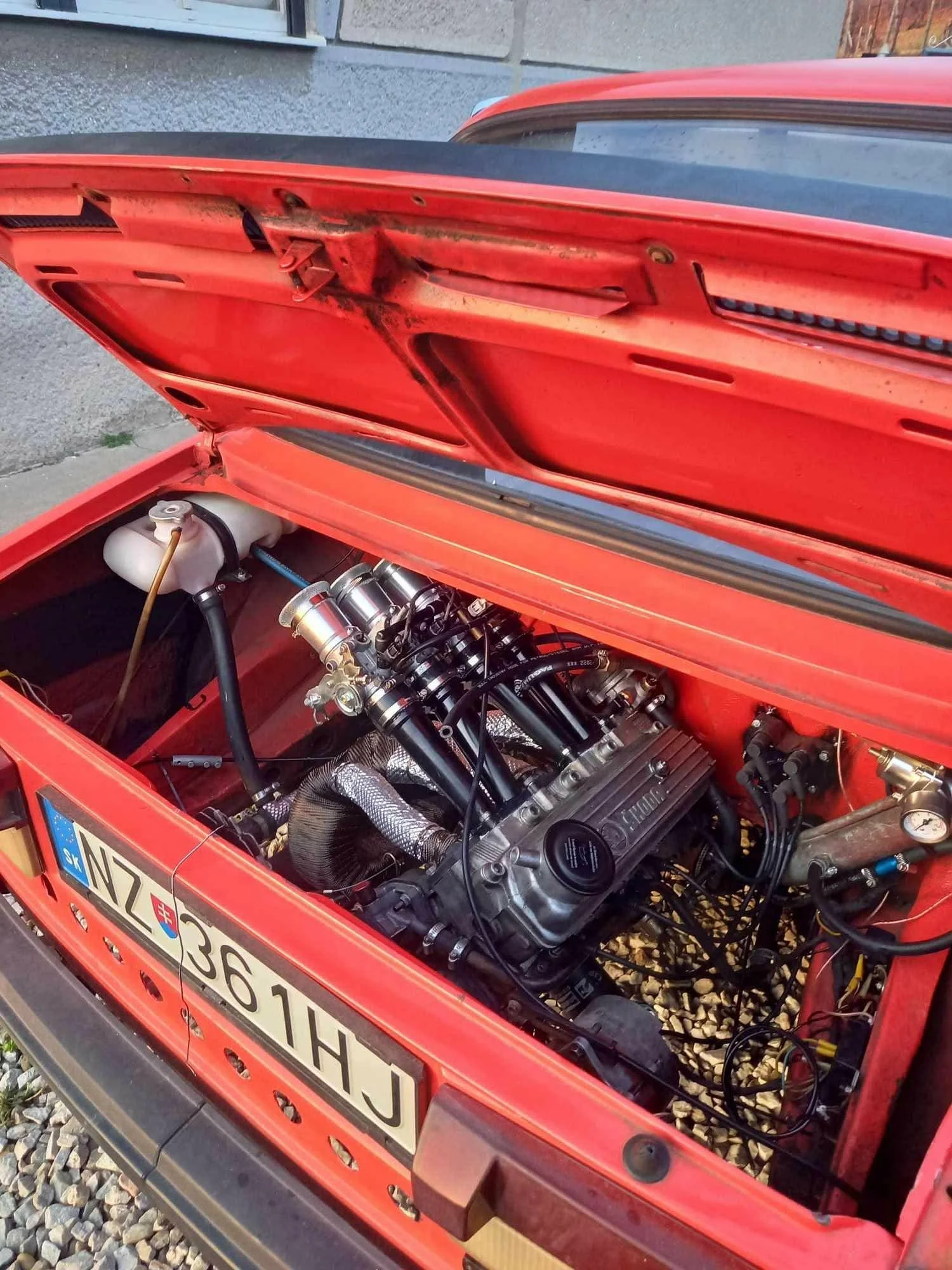 Close-up view of a red race car with its hood open, revealing the engine and mechanical components inside.