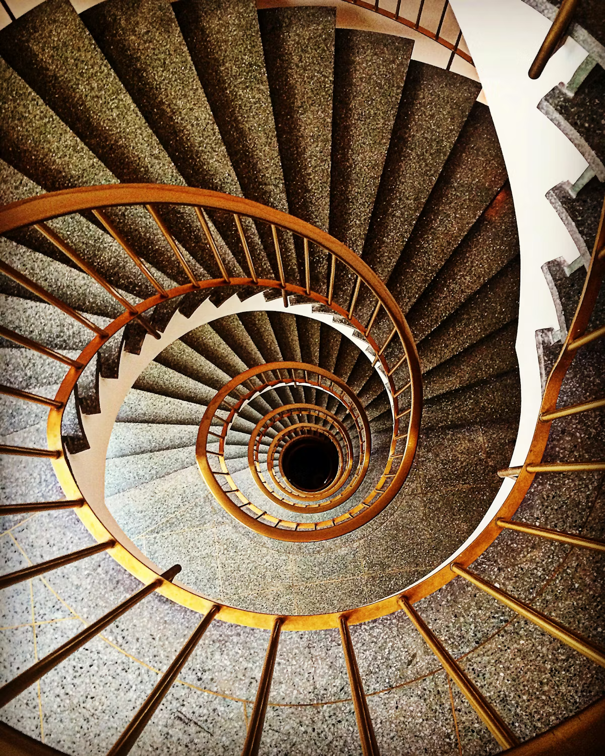 Spiral staircase viewed from above, with wooden handrail and carpeted steps.