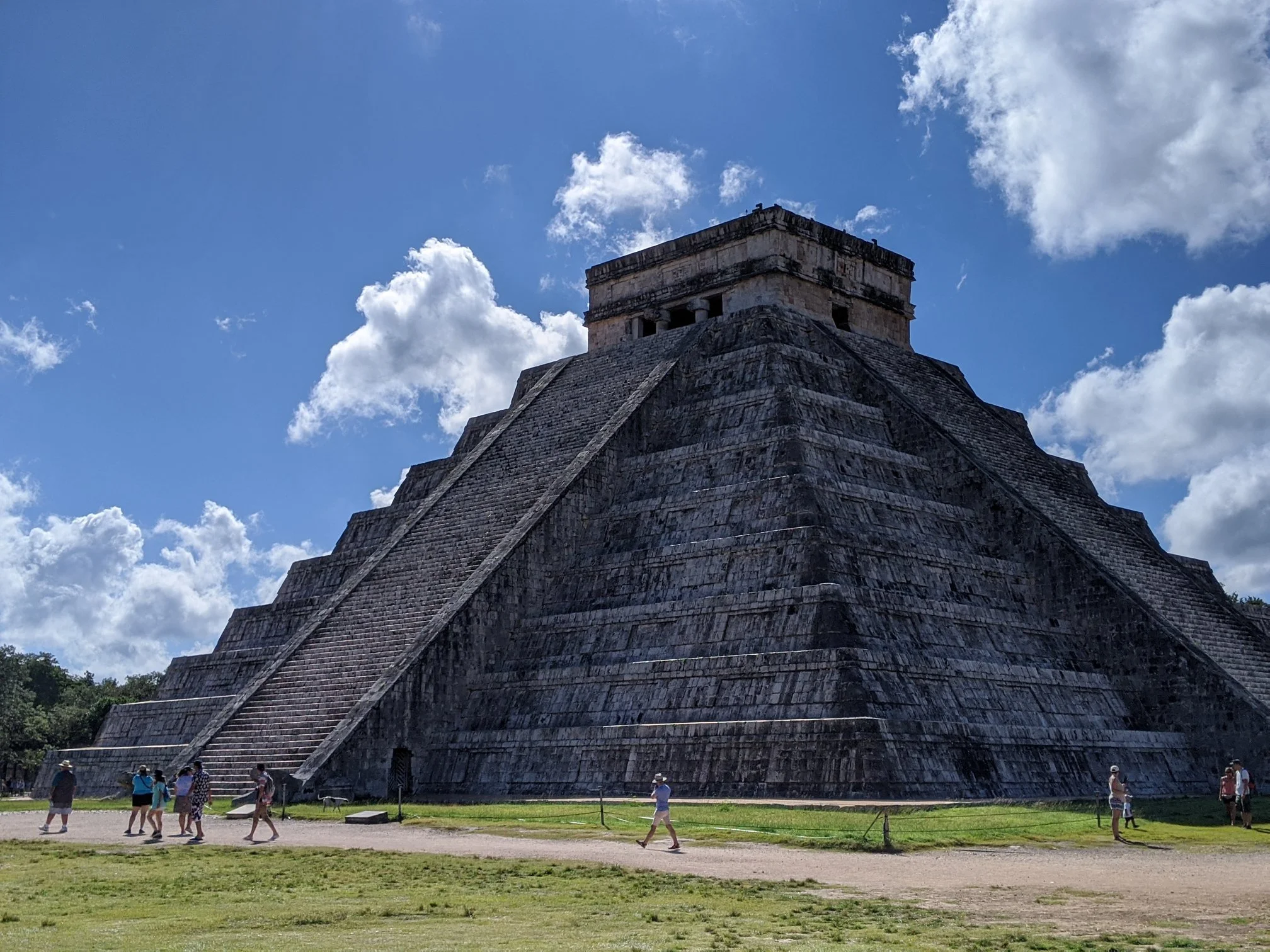 Chichen Itza pyramid under a partly cloudy sky with people walking at its base.
