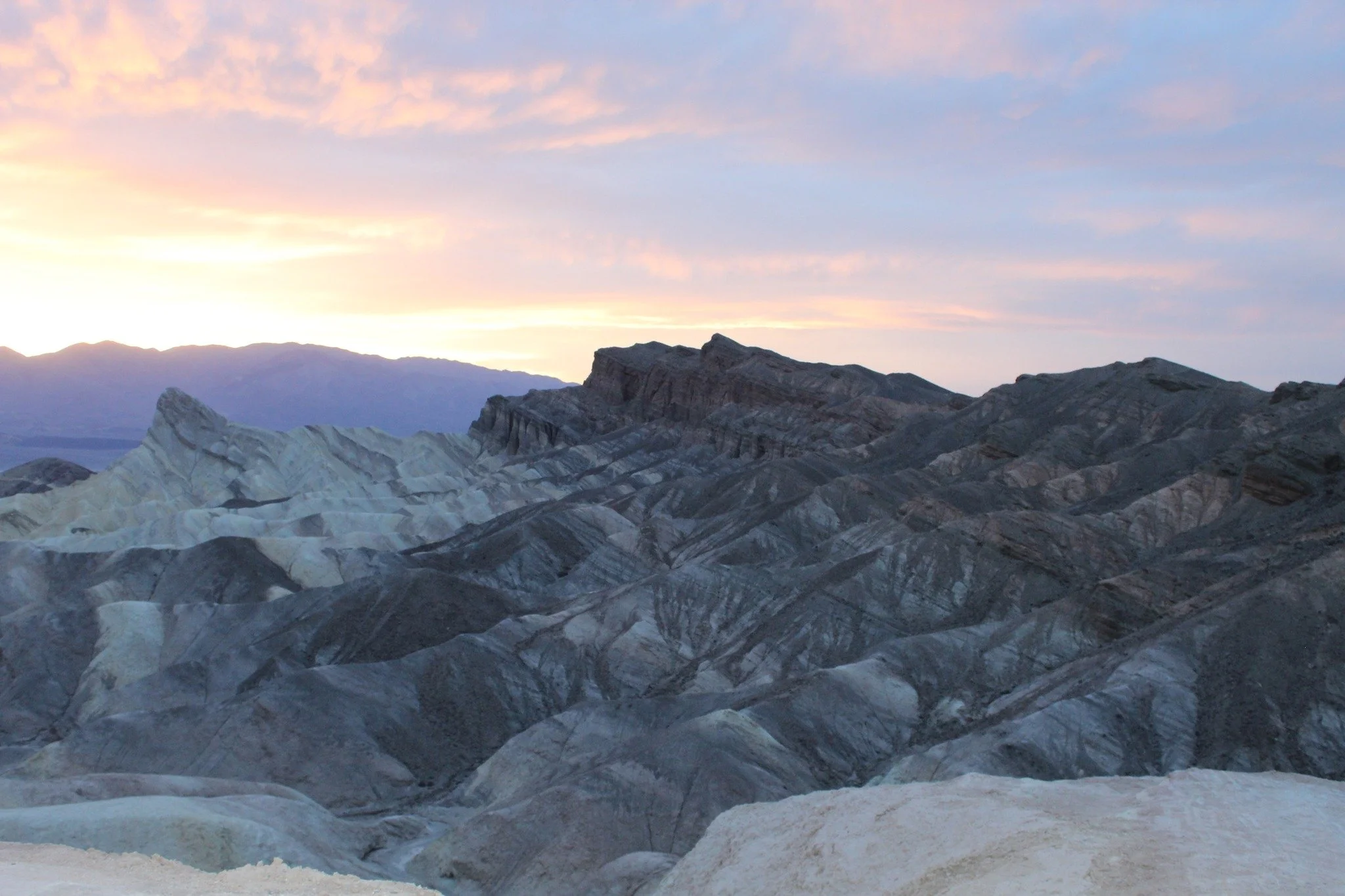 A landscape of layered, dark rocky mountains under a pastel-colored sky at dusk.