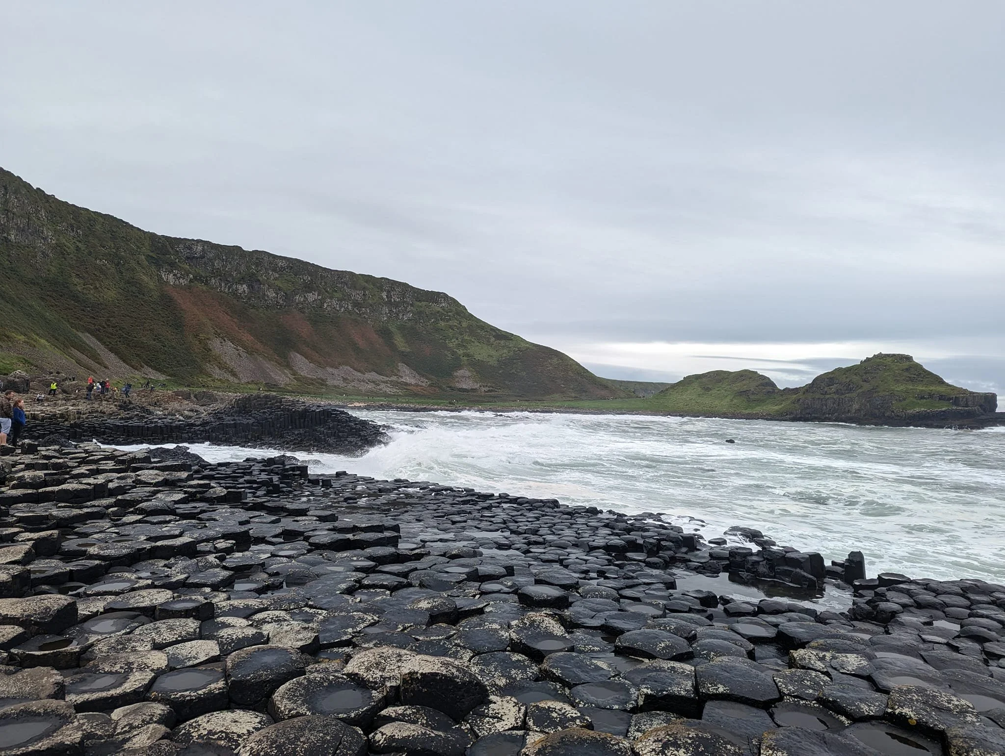 Famous basalt columns at the Giant's Causeway along the coast, with cliffs in the background and cloudy sky overhead.