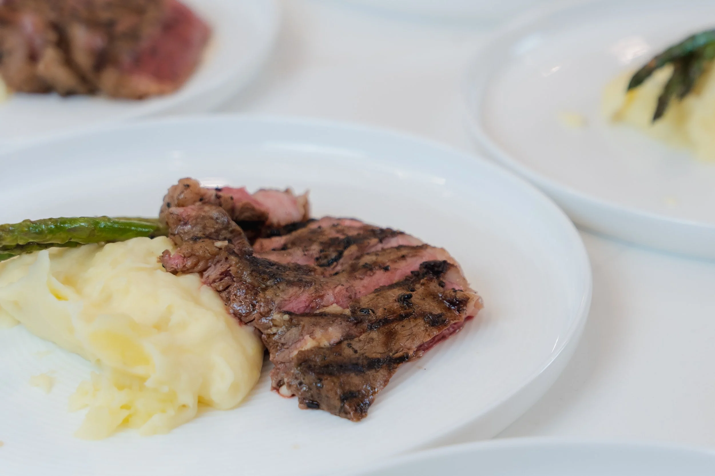 Grilled steak with mashed potatoes and asparagus on a white plate.