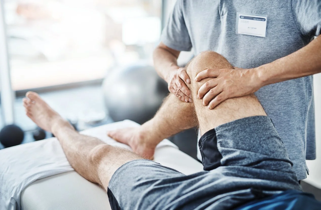 Physical therapist or chiropractor performing a knee massage or assessment on a man's leg in a clinical setting.