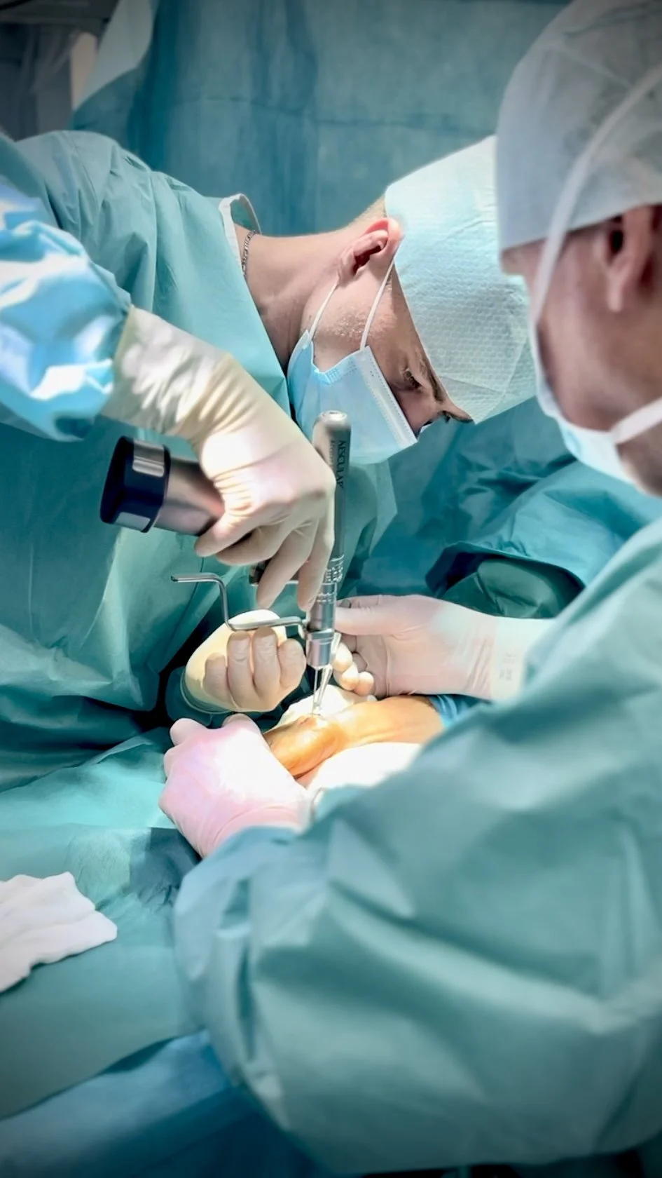 Two surgeons performing a medical procedure in an operating room, focusing on the patient’s mouth or face.