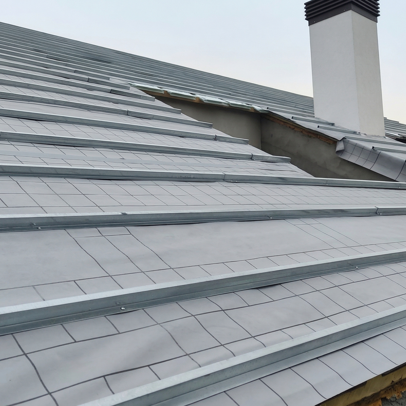 Installed solar panels on a sloped roof of a house with a chimney in the background.