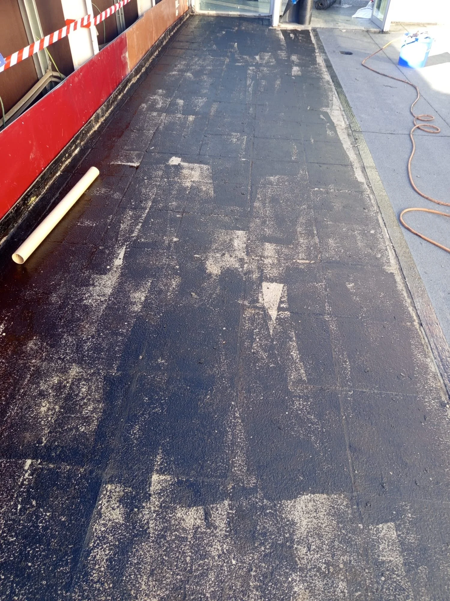 Construction site floor being prepared, with black asphalt and white powder, with construction tools and safety barriers visible.
