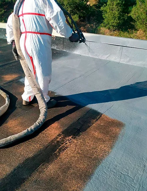 A worker in protective gear spray painting a roof surface to create a waterproof seal.