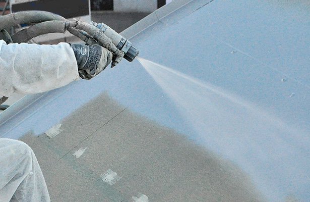 Close-up of a person spraying a protective coating or paint on a curved surface with a sprayer.