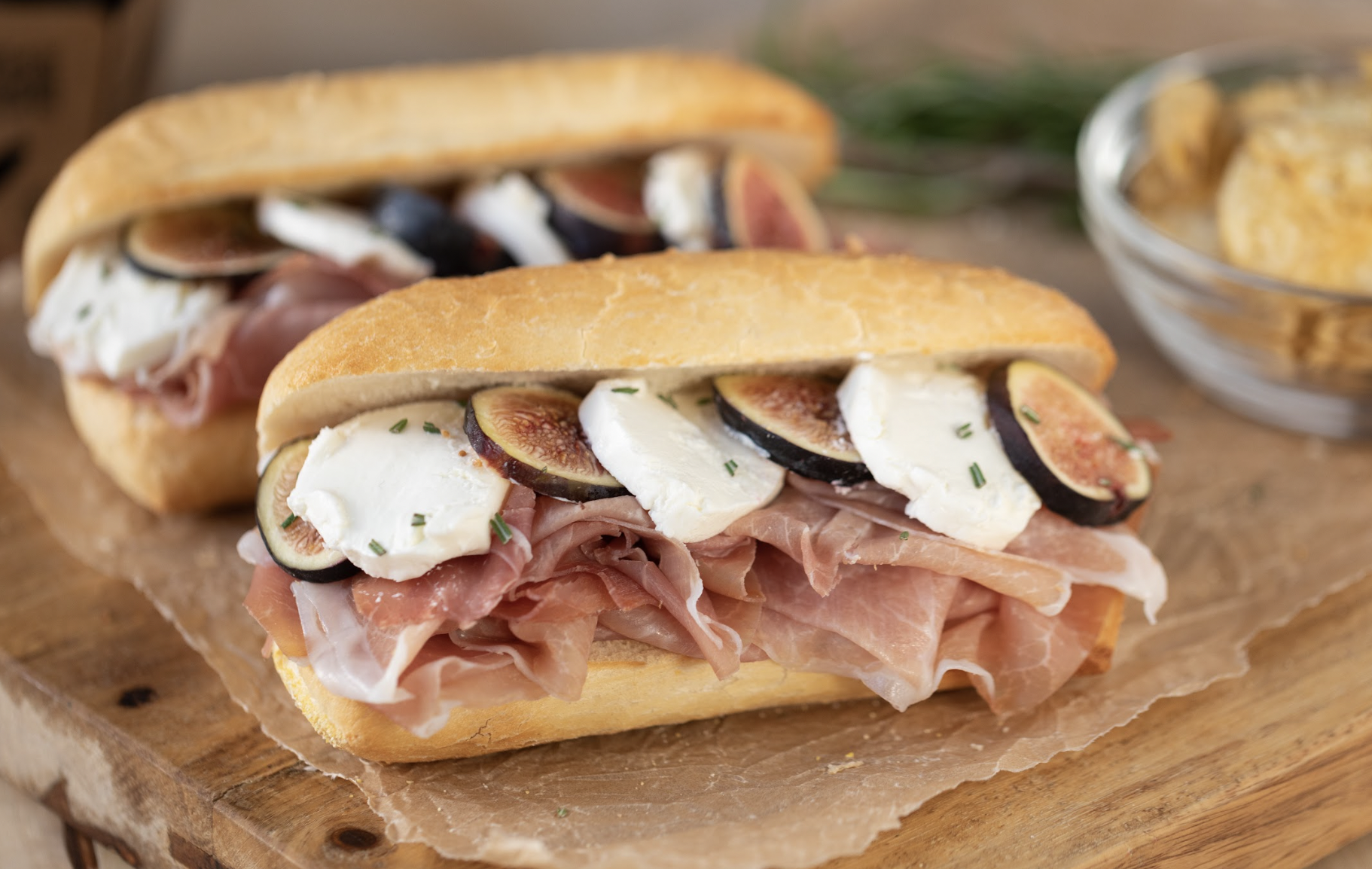 Bread rolls filled with prosciutto, fresh figs, and mozzarella cheese served on a wooden surface.