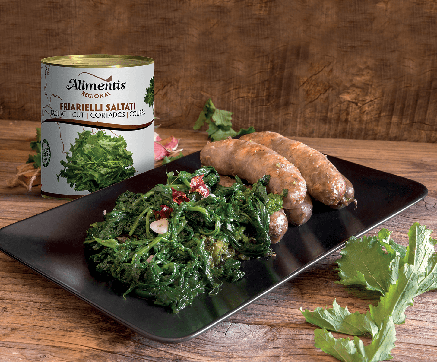 A plate with cooked sausage links, sautéed kale, and a can of salted anchovies on a wooden surface.