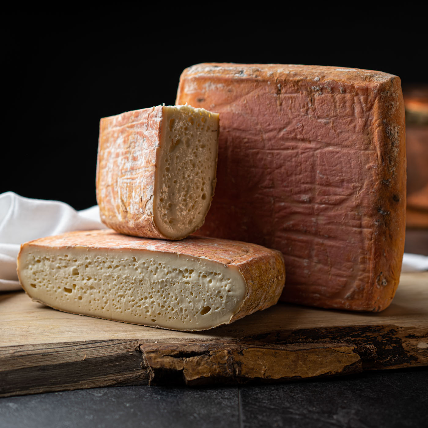 A close-up of a block of cheese with two slices cut, placed on a wooden board against a black background.