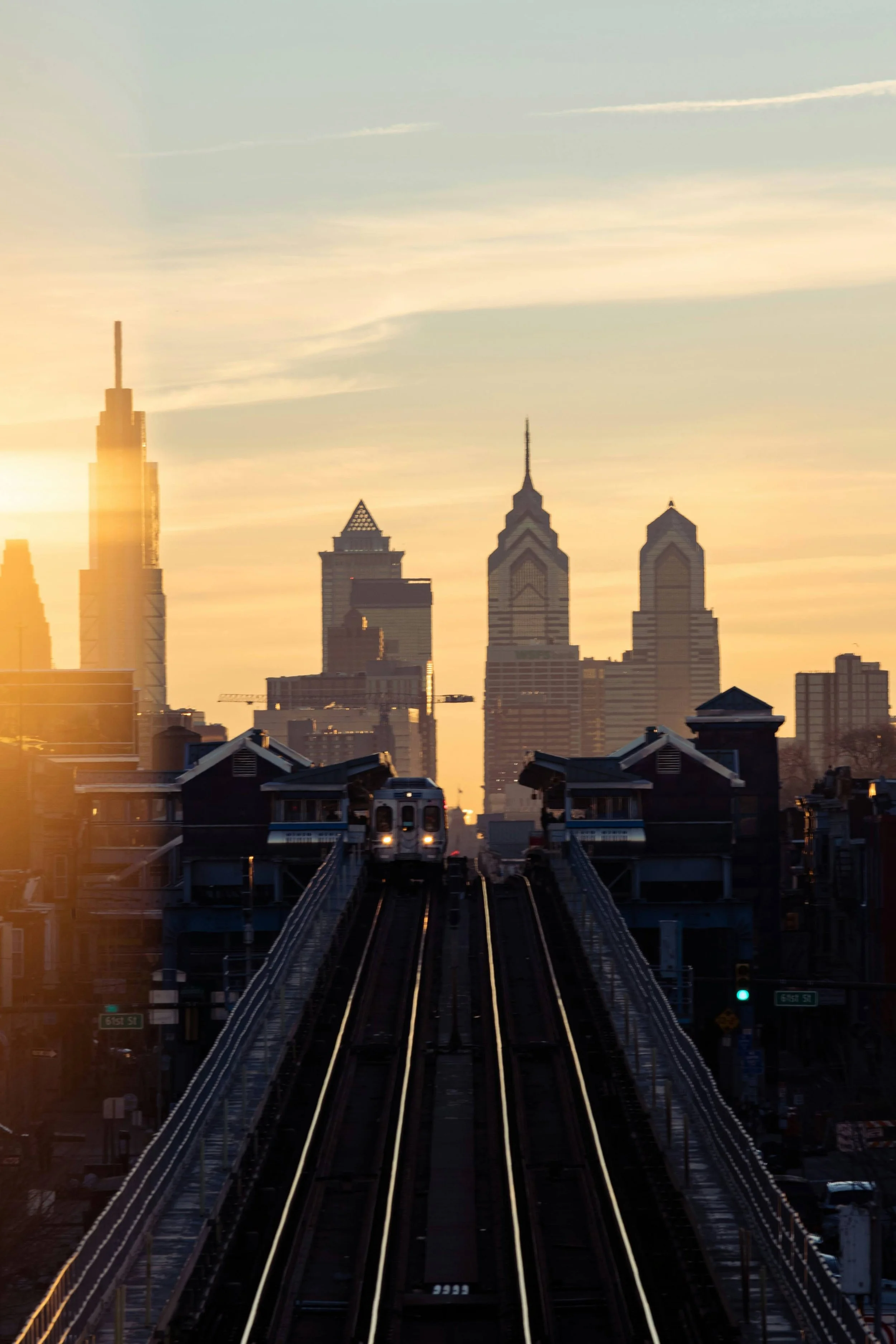 The L travels westbound, with sun; haze; and city as a backdrop.