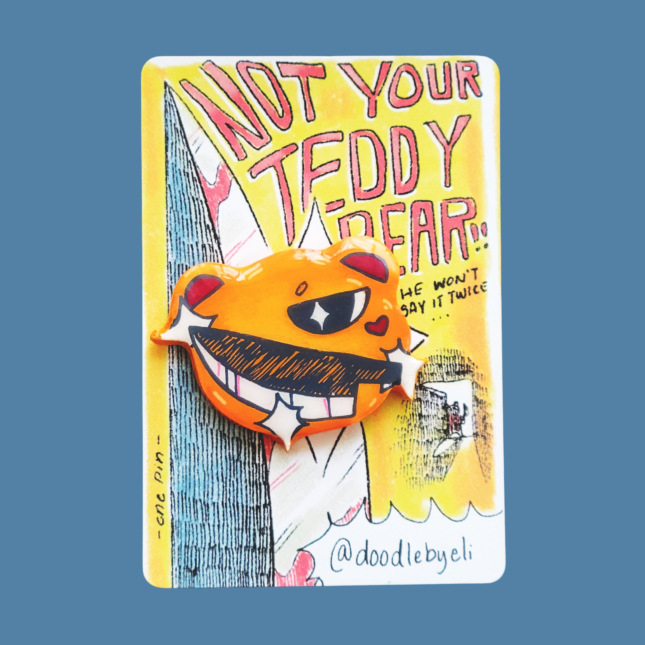 A colorful teddy bear with a knife pin is attached to a card. The card has text that says 'Not Your Teddy Bear.. he won't say it twice,' and features artistic drawings and signature.