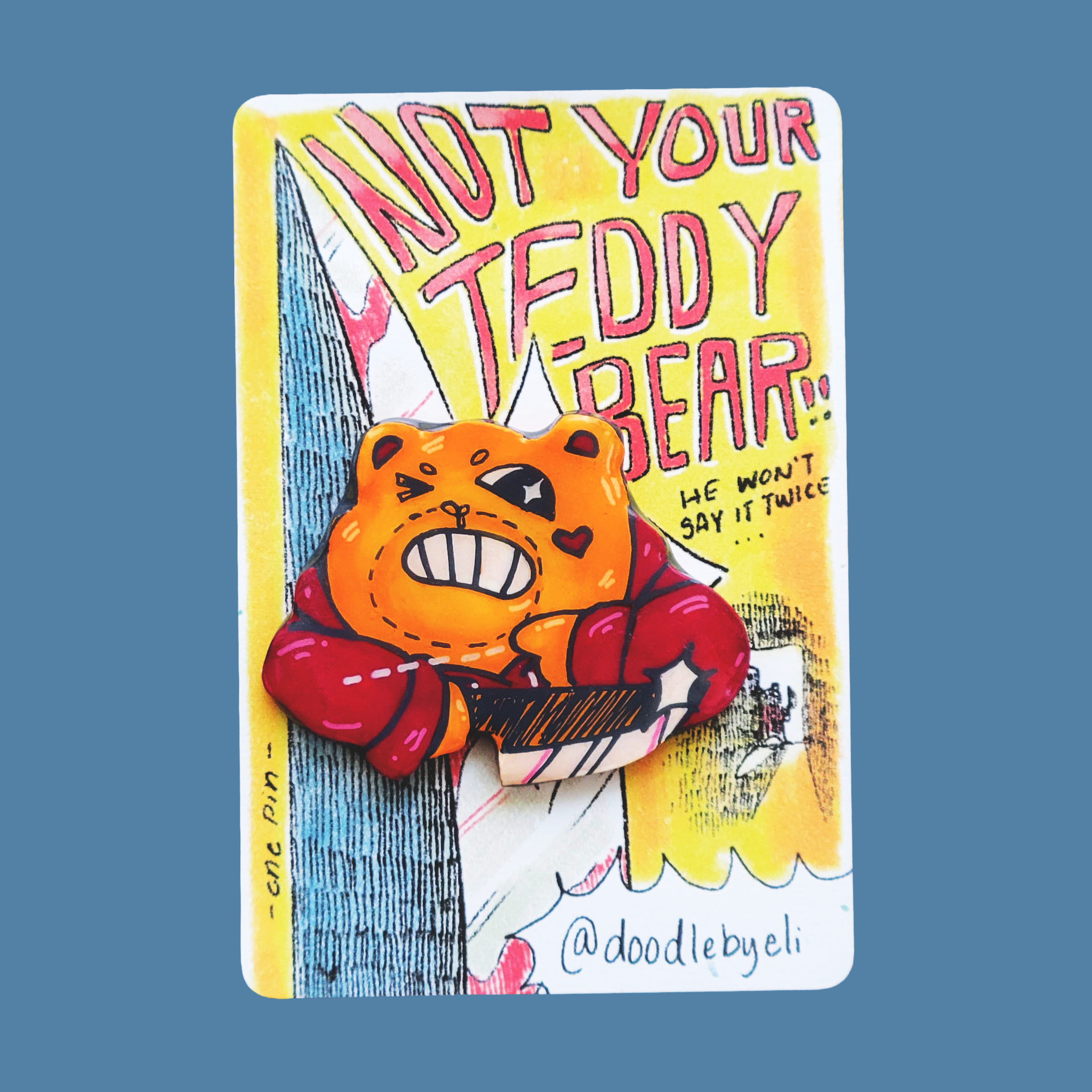 A colorful teddy bear with a knife pin is attached to a card. The teddy bear is making a motion with its hand across its neck. The card has text that says 'Not Your Teddy Bear.. he won't say it twice,' and features artistic drawings and signature.