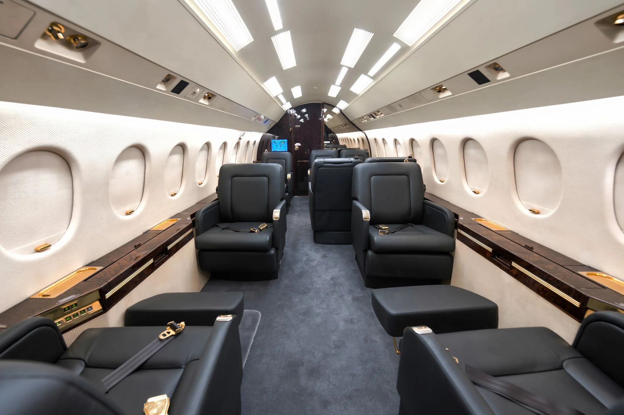 Interior of a private jet with black leather seats, arranged in pairs with a central aisle, small windows on each side, and overhead compartments above.