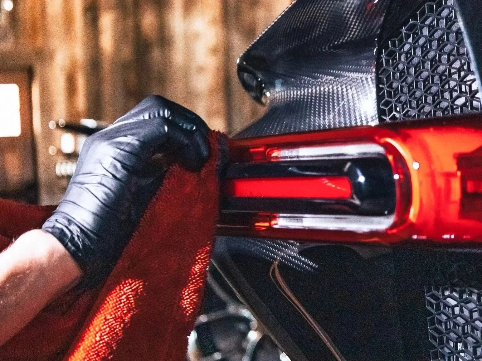 A person in a black glove is polishing or detailing the tail light of a Bugatti with a red cloth.