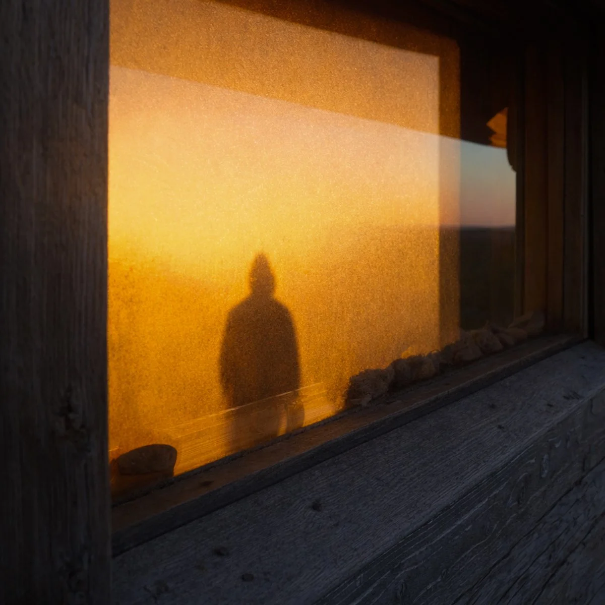 Ikkunan heijastuma, jossa henkilön varjo kuivalla seinustalla auringonlaskun aikaan.