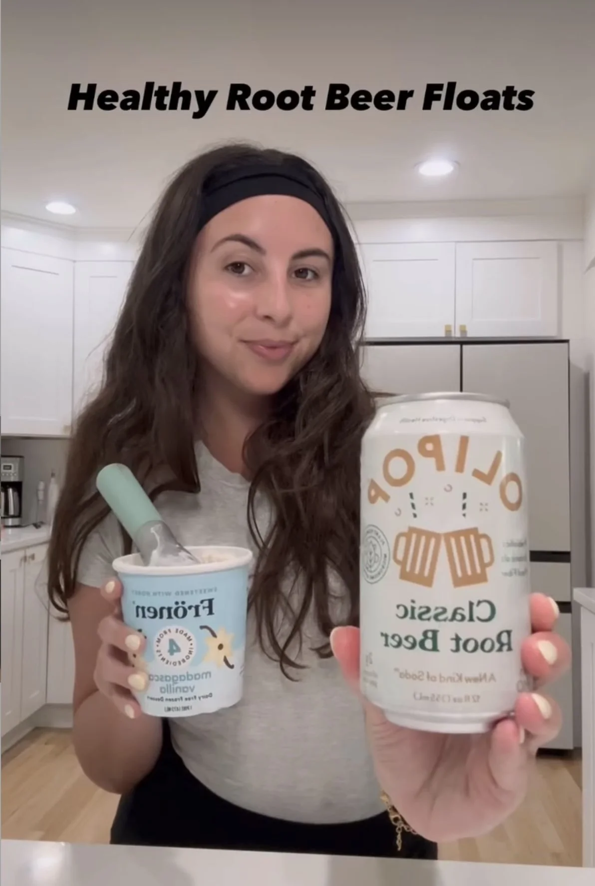 Woman holding a can of Clarssic Root Beer and a cup of Ice Cream with a Root Beer float, in a kitchen.