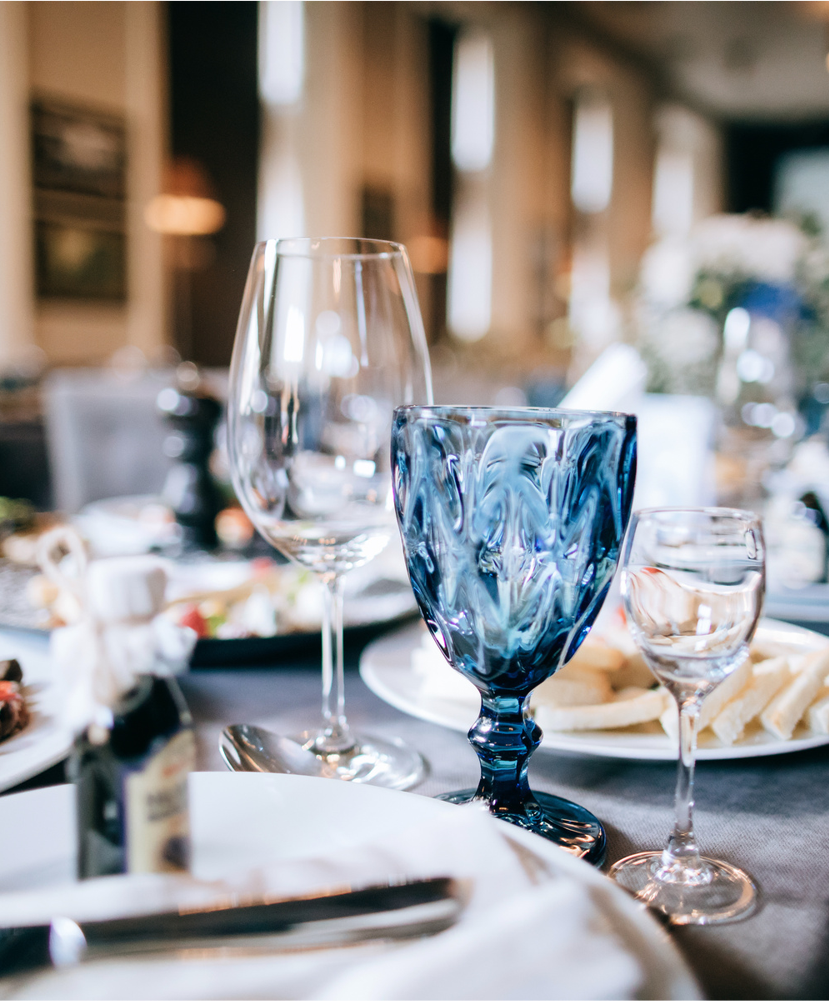 Close-up of elegant glassware on a table at a formal dining event, with plates and food in the background.