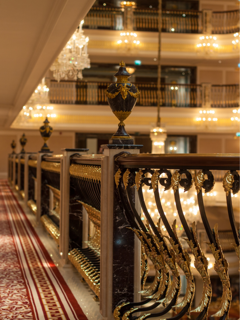 Luxurious hotel interior with a black and gold ornate railing, crystal chandeliers, and multiple levels of balconies.