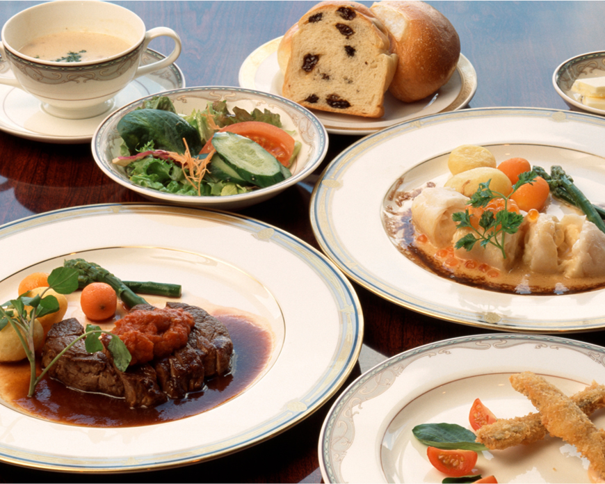 A table with various dishes, including salad, bread, soup, a beef main course with vegetables and sauce, a seafood dish with sauce, and fried items with garnish.
