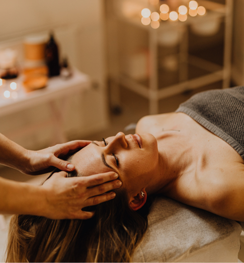A woman receiving a facial massage in a spa room with soft lighting and candles.