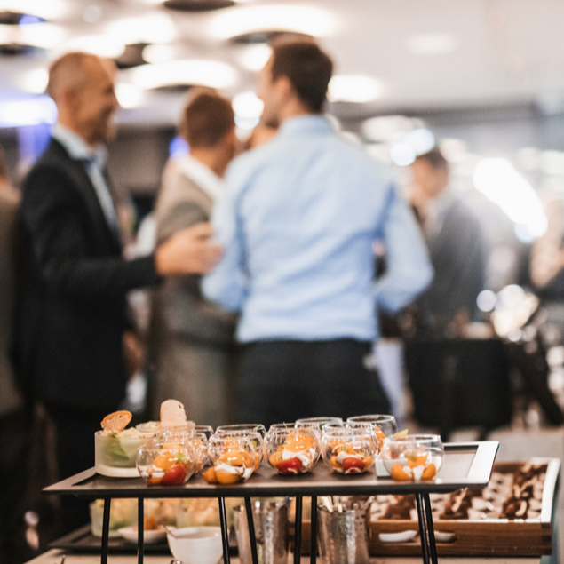 Appetizers and desserts on a tray at a social event with blurred people in the background.