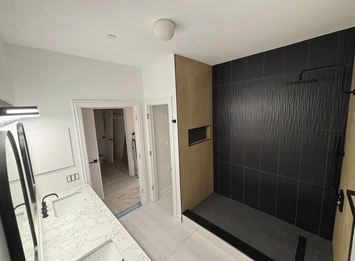 Bathroom with a black tiled walk-in shower, white walls, a marble countertop with a sink, and a doorway leading to a walk-in closet.