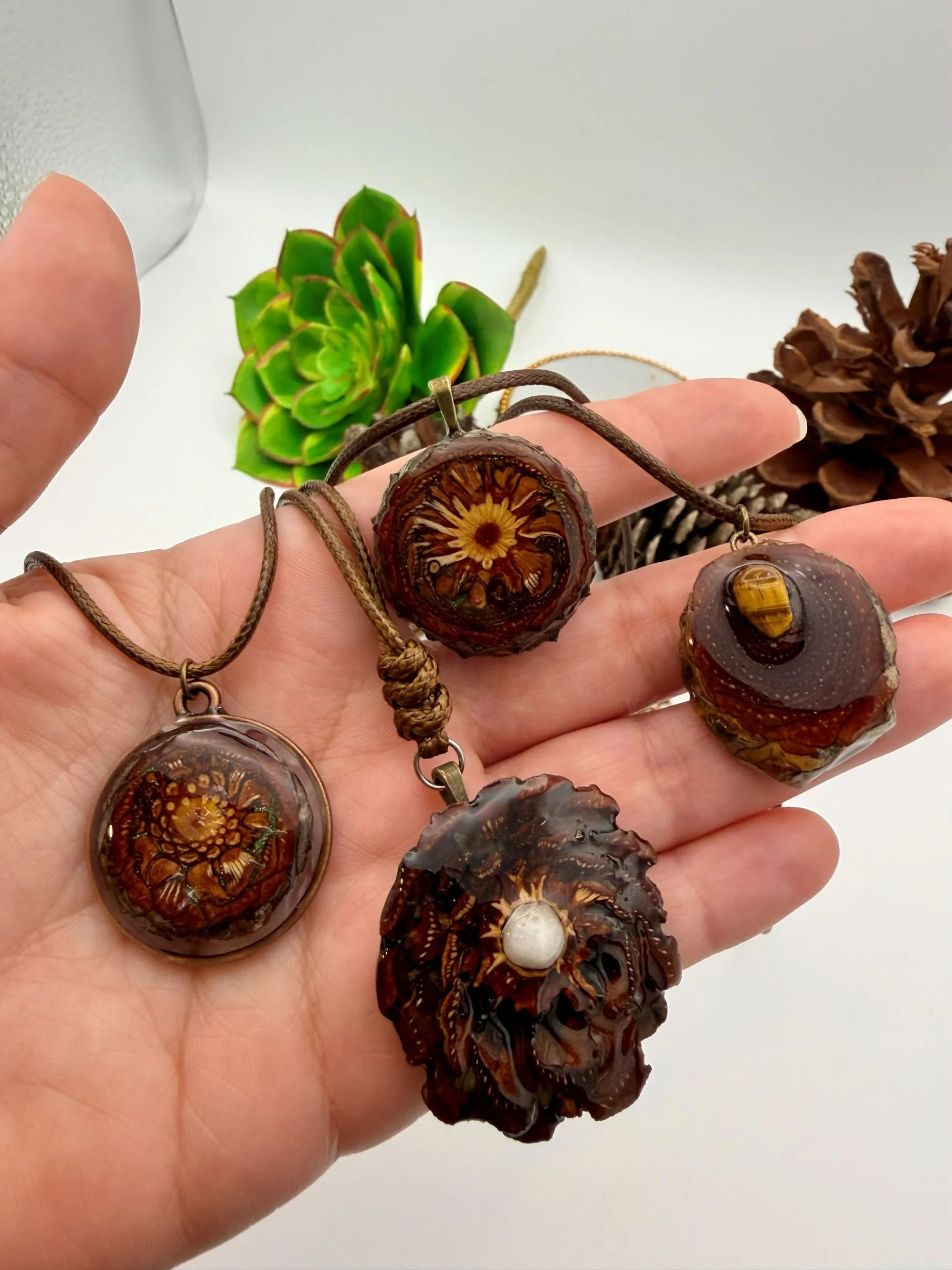 Collection of four carved agate necklaces with intricate designs, laid on a person's hand, with succulent plants in the background.