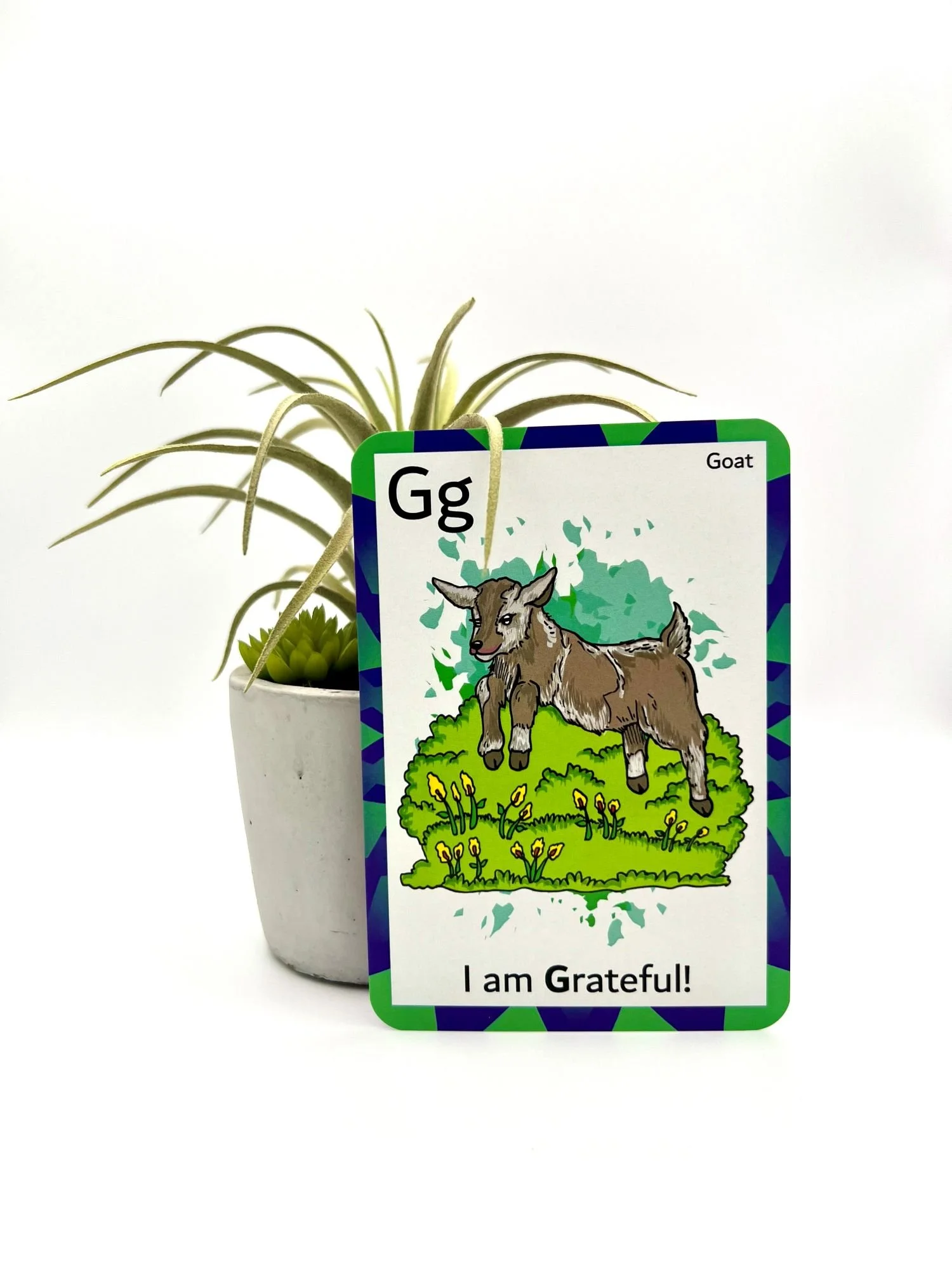 A potted succulent plant holds a colorful card featuring a cartoon goat, the letter Gg, and the words 'I am Grateful!'