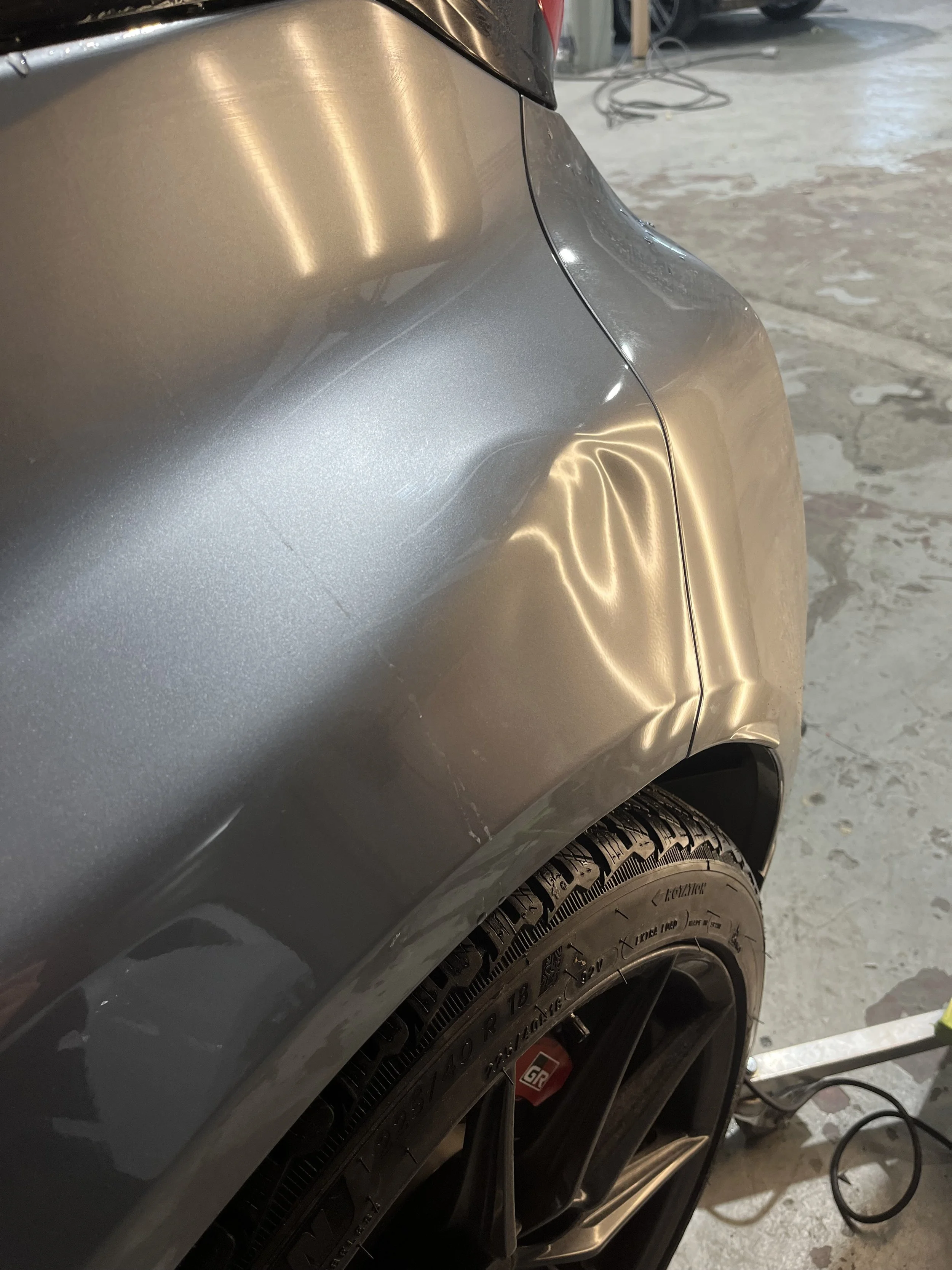 Close-up of a silver car's rear wheel and fender with a dent and some scratches on the body.