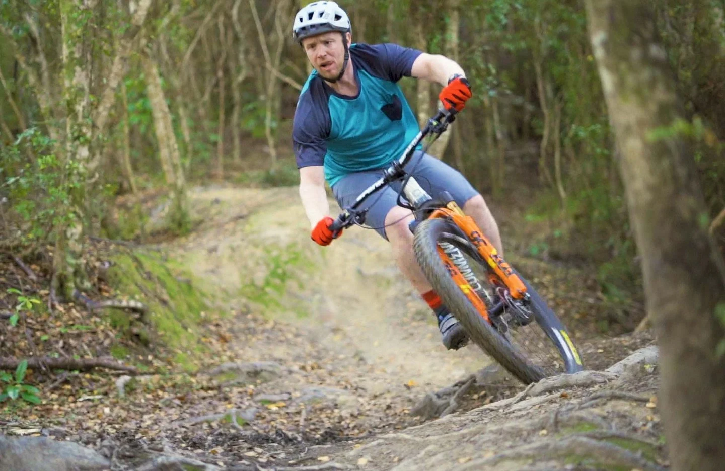 A man with a helmet riding an orange mountain bike down a dirt trail in Wainuiomata Mountain Bike Park