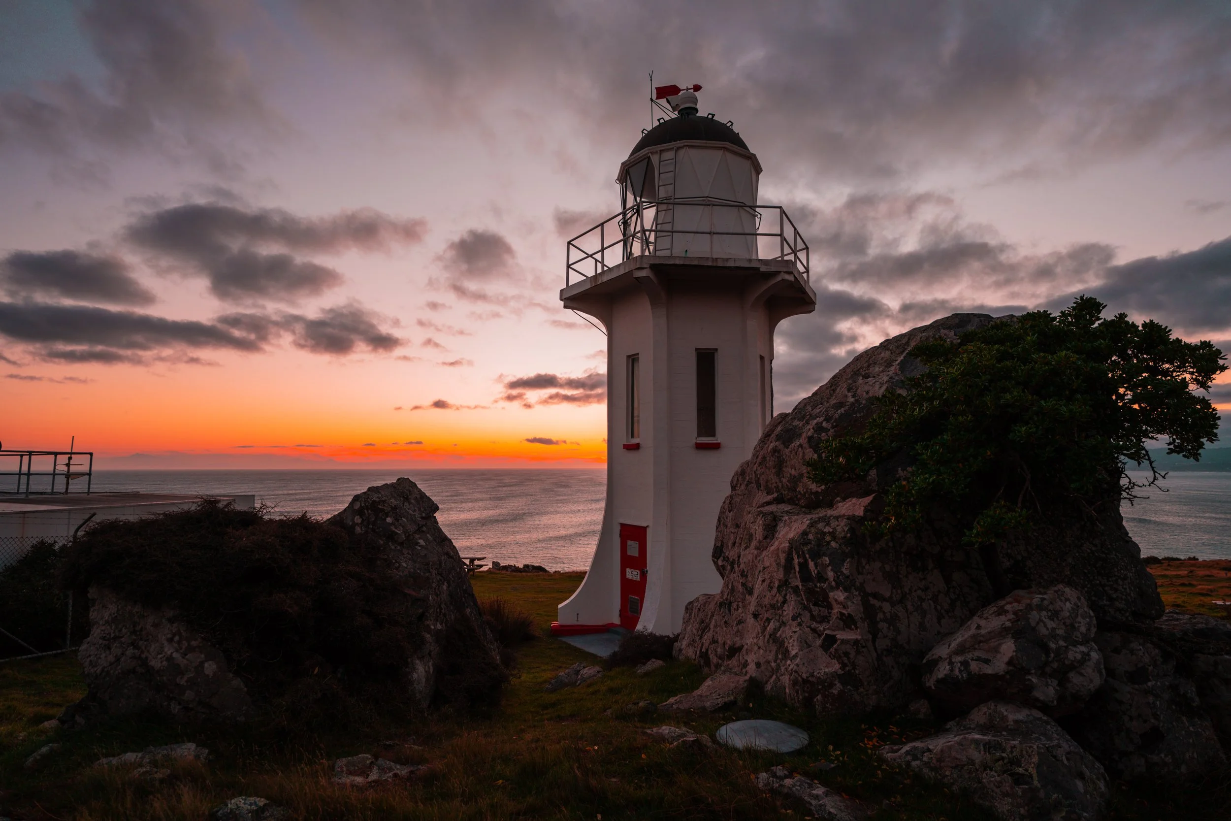 A vibrant sunset occurs behind the Baring Head Lighthouse, located in Wainuiomata