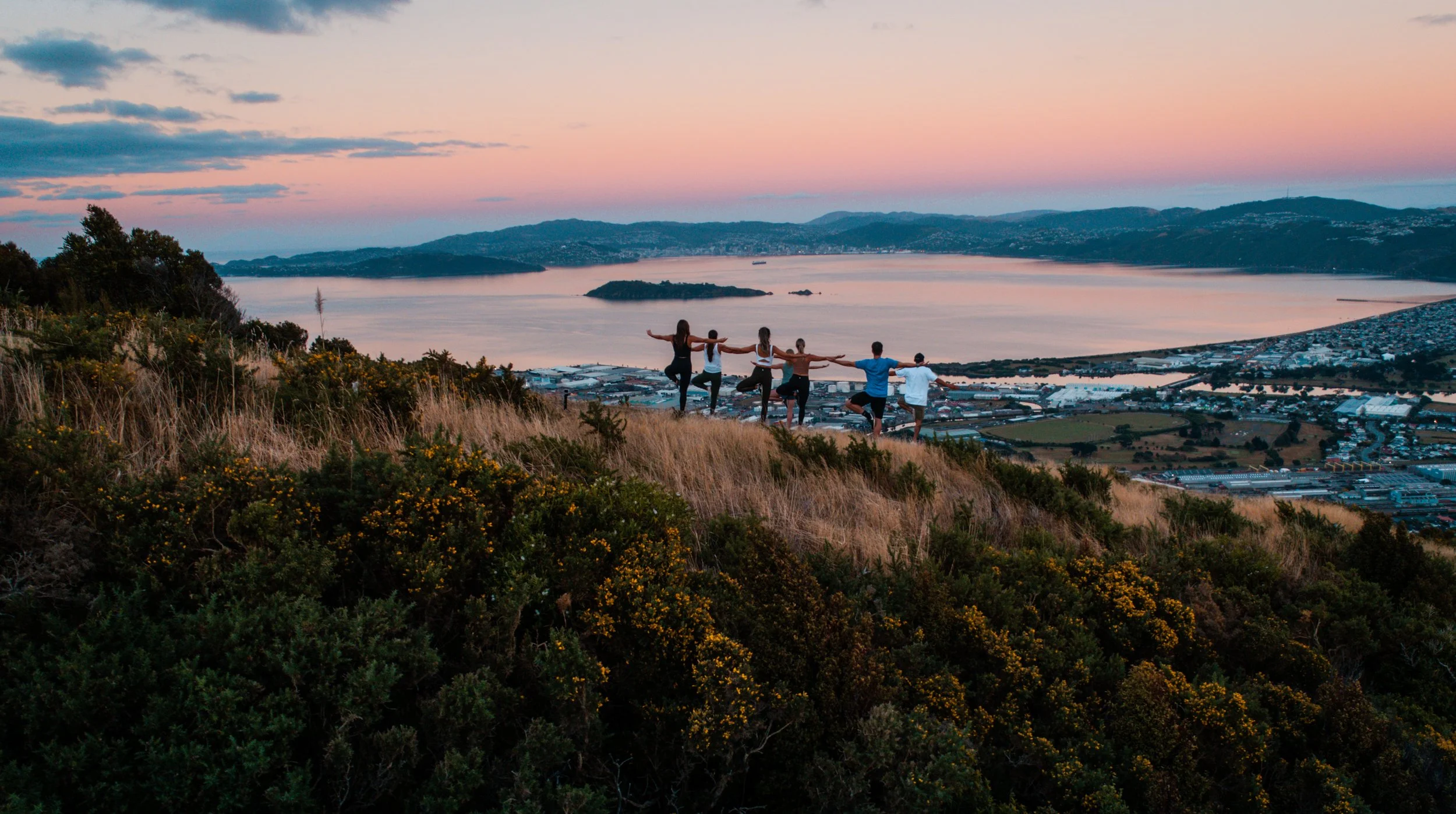 Several people do a yoga pose on top of a hill during sunrise in Te Whiti Riser, located in Lower Hutt Wellington