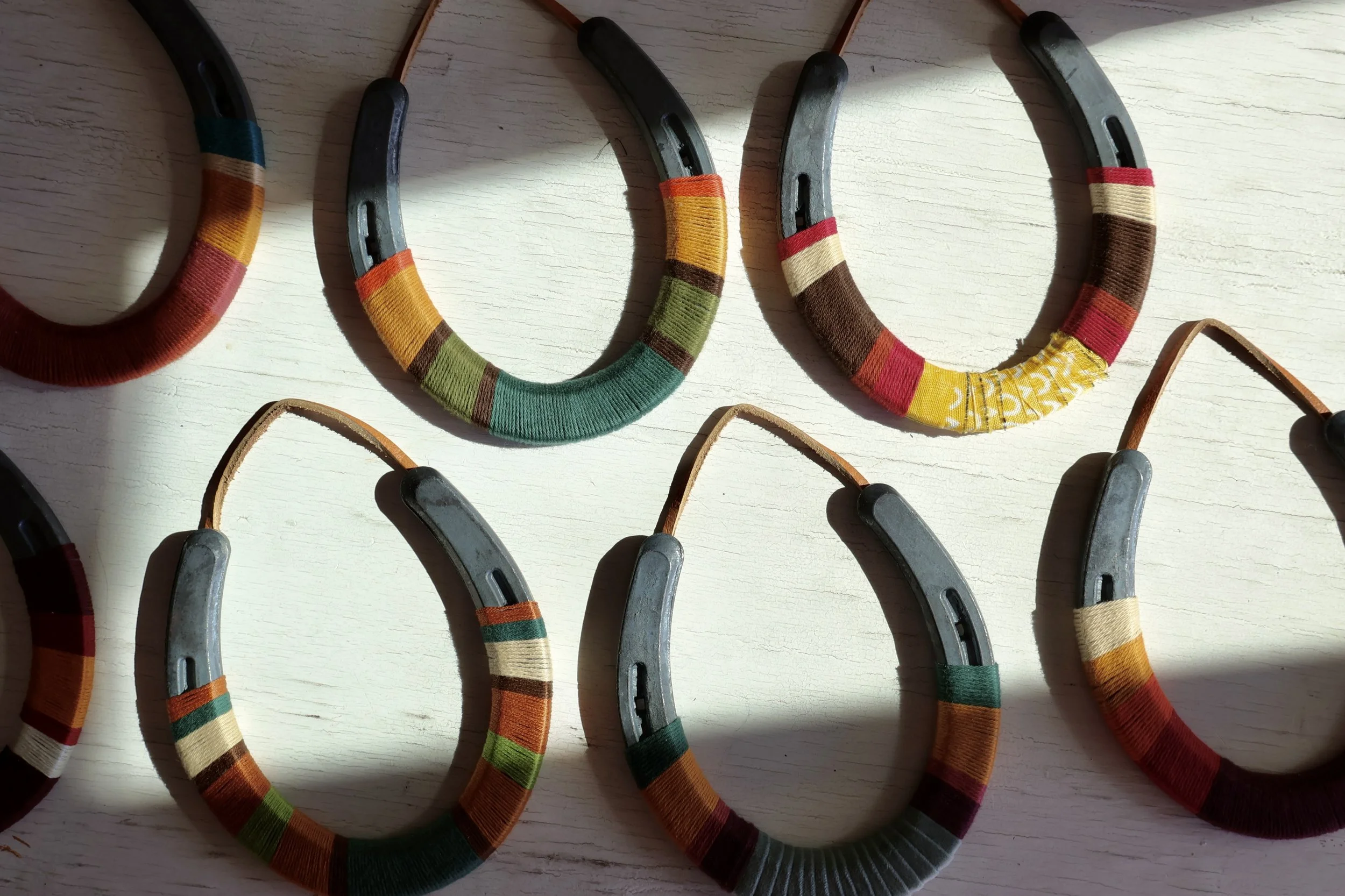 Multiple horse halters with colorful woven fabric covers on a light wooden surface.