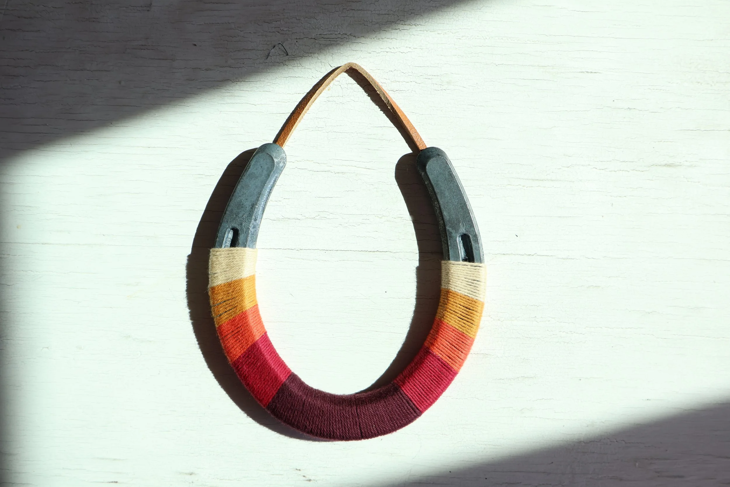 Colorful fabric-covered horseshoe with metal ends, placed on a white wooden surface with sunlight casting shadows