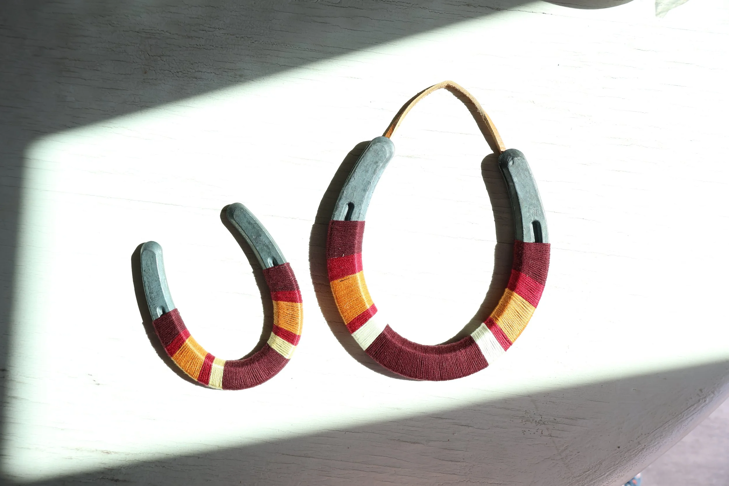 Three horseshoe-shaped objects with red, yellow, and white striped fabric coverings on a white wooden surface, cast in partial sunlight.