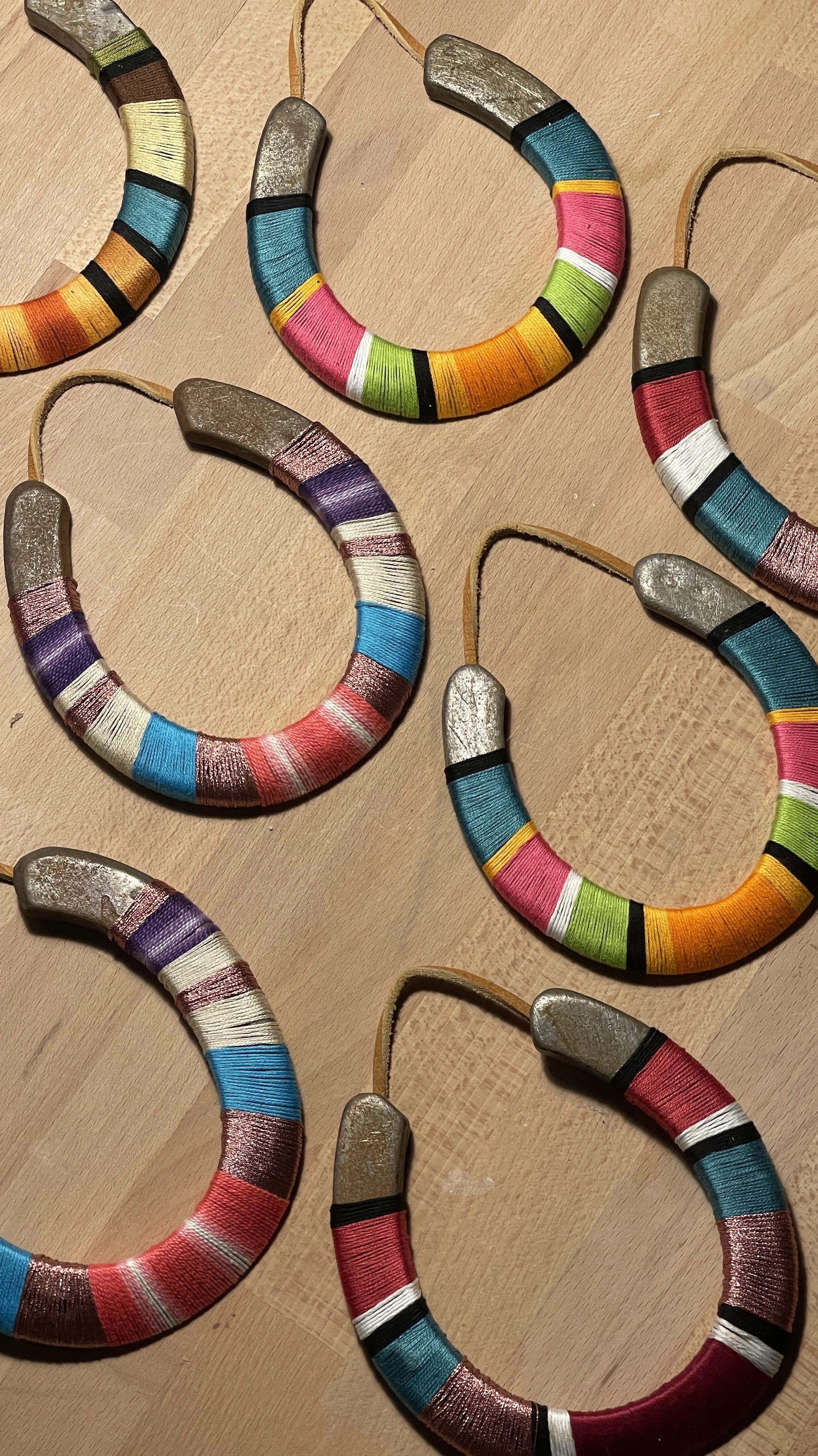 Colorful, wrapped hoop earrings with metallic tops arranged on a wooden surface.