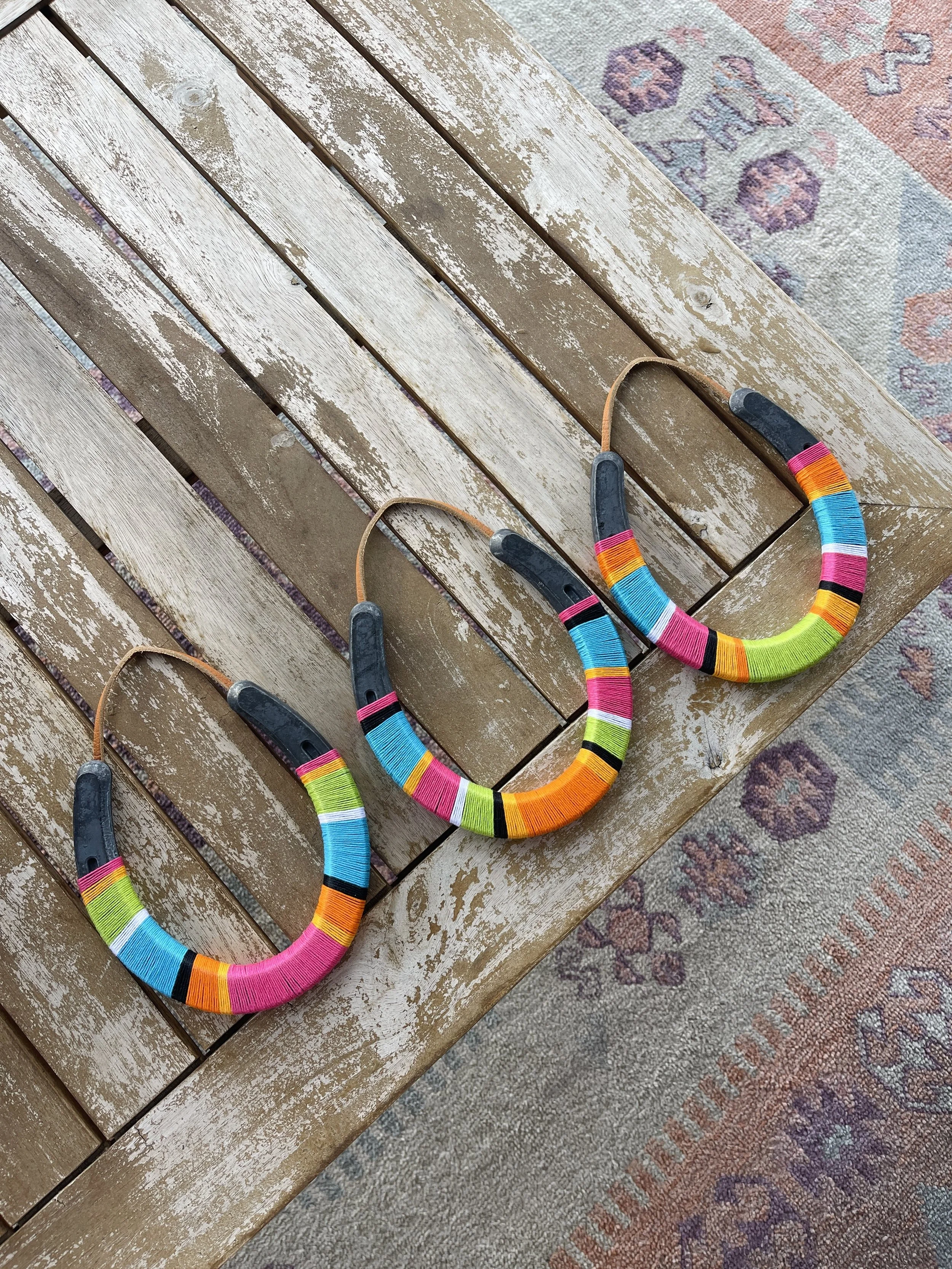 Three colorful necklaces with black plastic clasps are laid on a weathered wooden table, partially on a patterned rug.