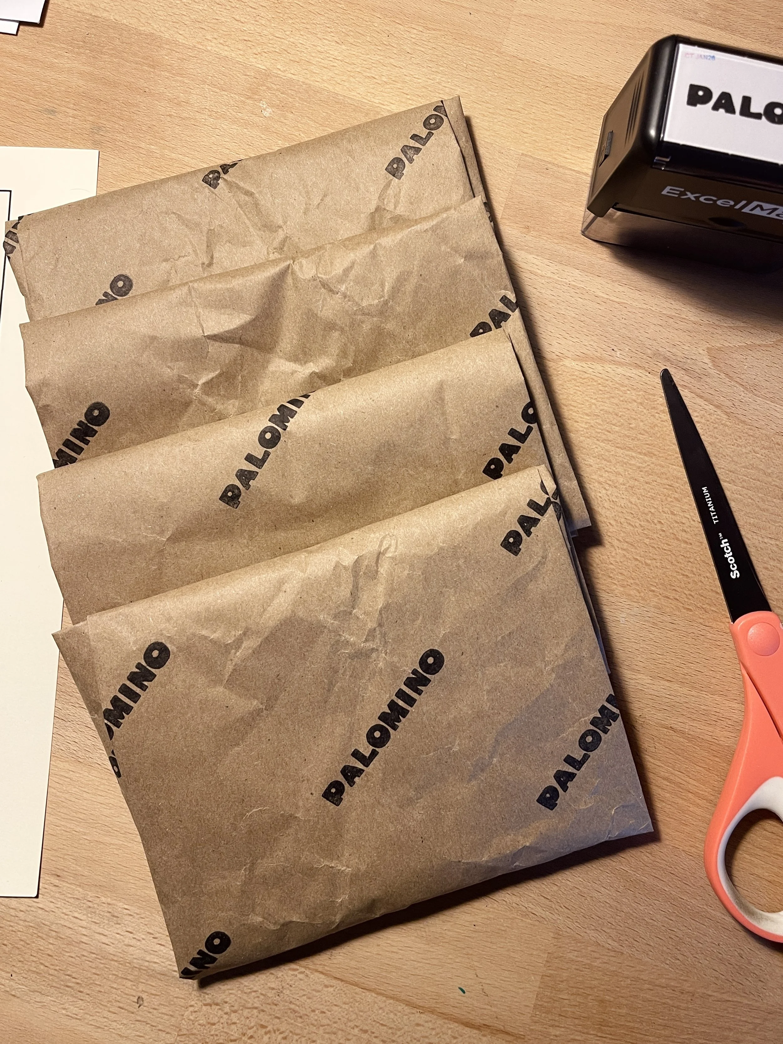 Three brown paper bags with 'PALOMINO' printed on them lying on a wooden table, with scissors positioned nearby.