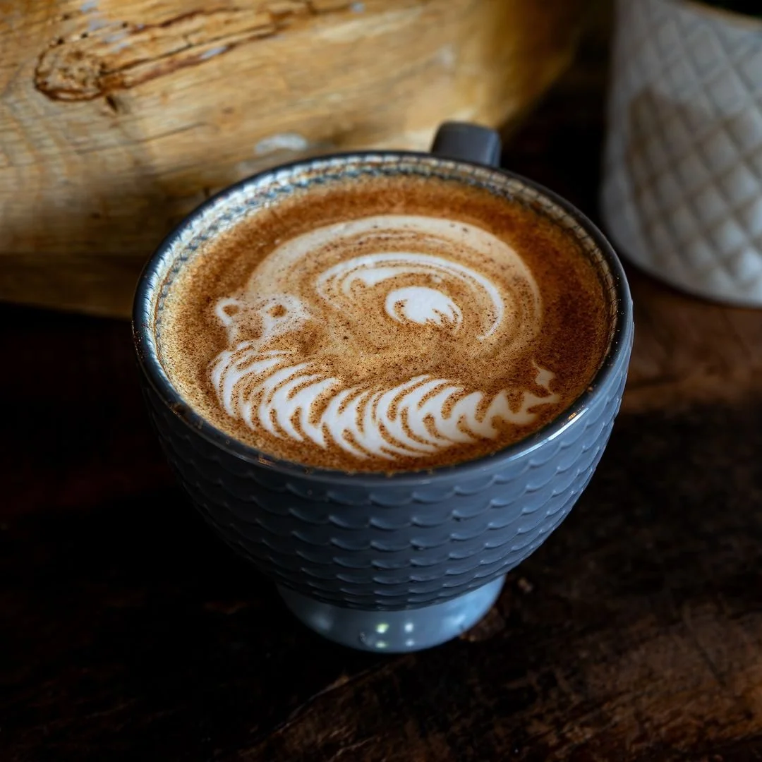 Close-up of a cup of latte with latte art in the shape of a bear, placed on a dark wooden surface.