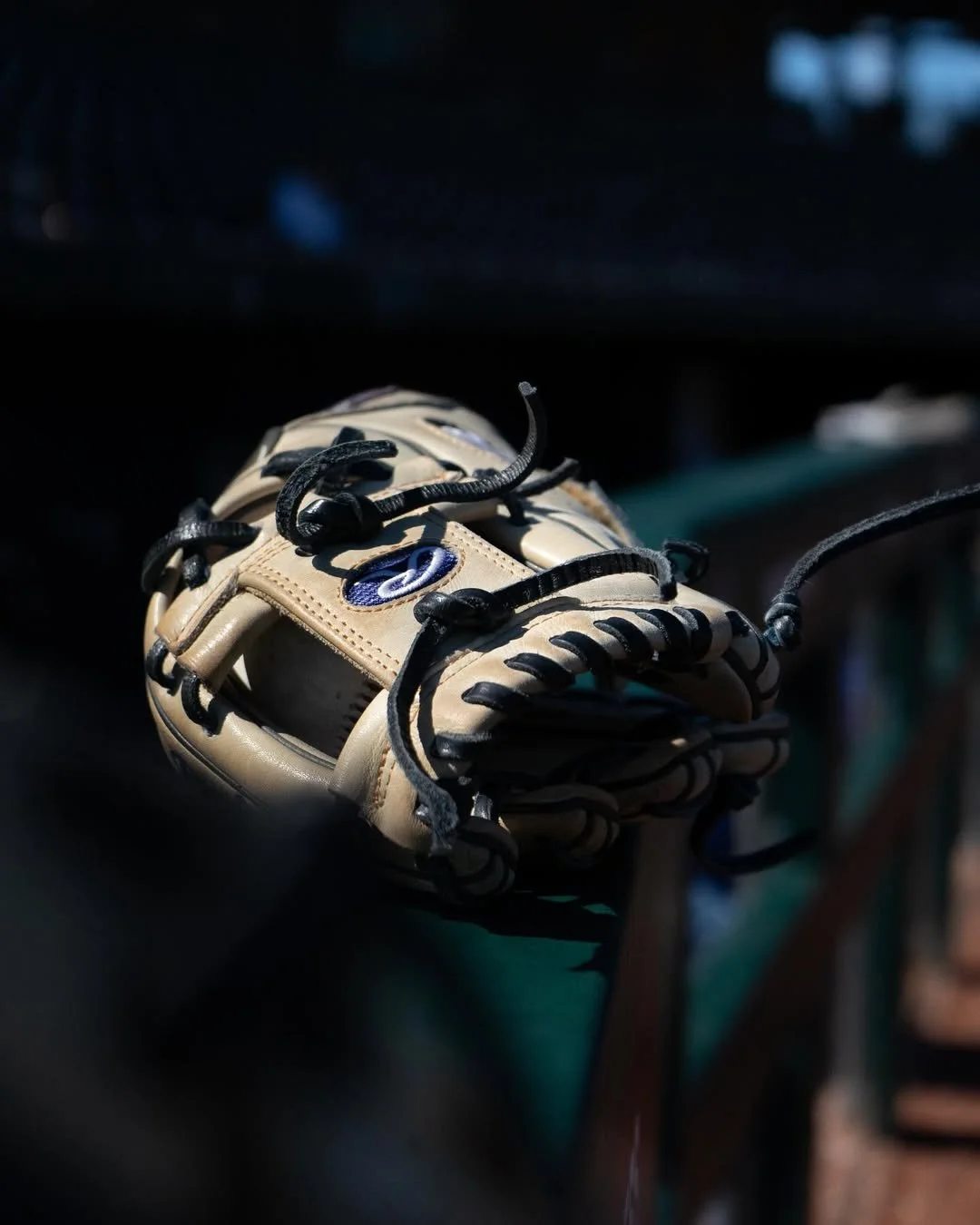 A beige baseball glove with black laces resting on a dark surface.