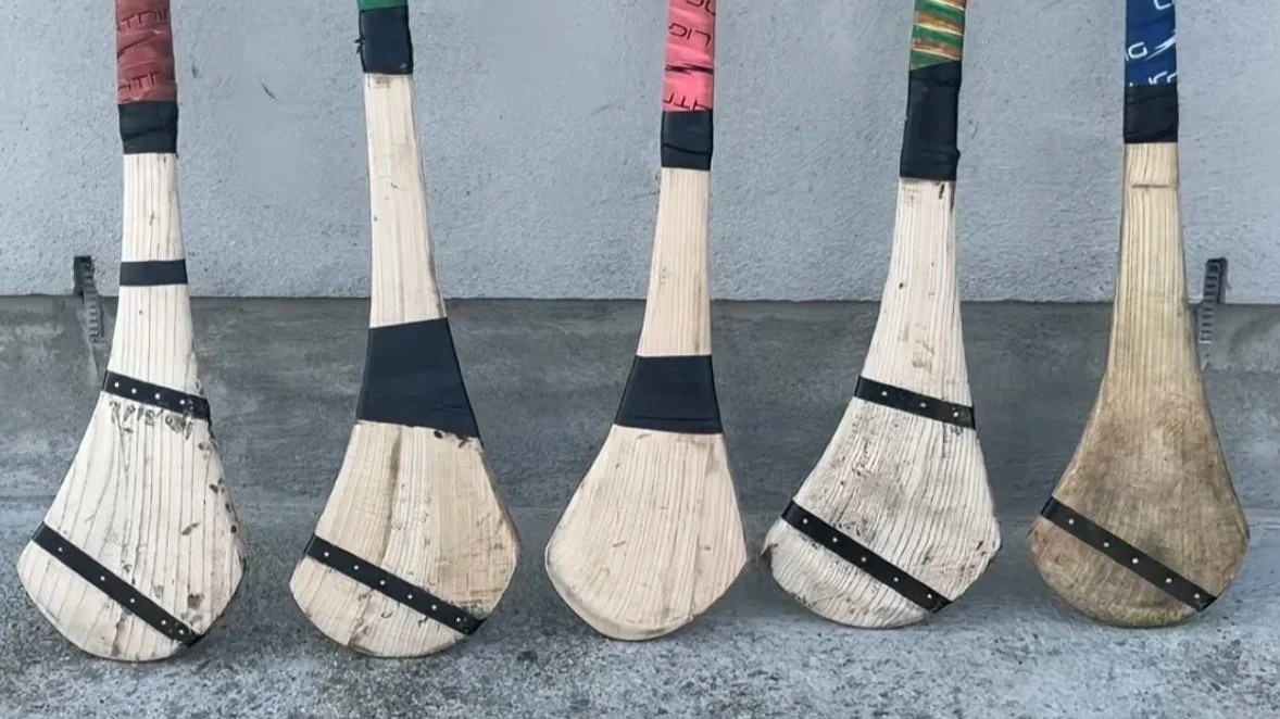 Five wooden hockey sticks with varying levels of wear, lined up against a wall.